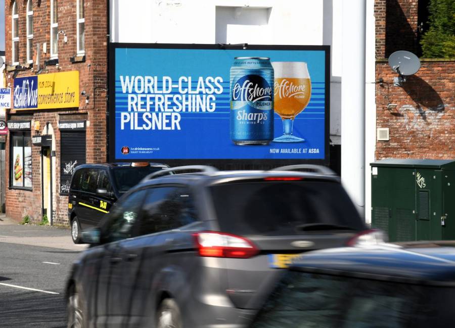 A beer advert displaying on a bright blue digital Billboard alongside traffic