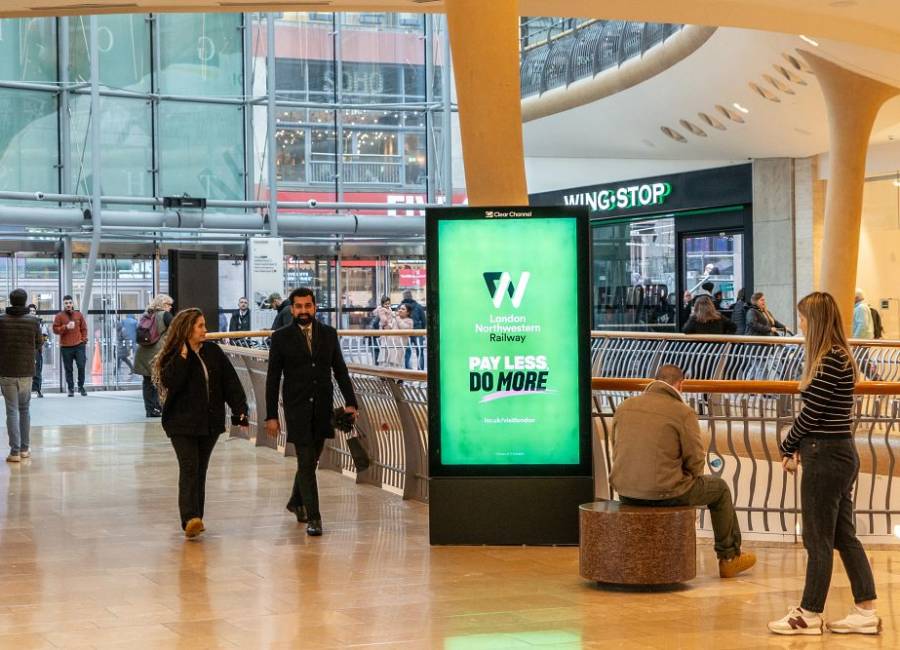 A green railway ad displaying on a shopping centre digital screen