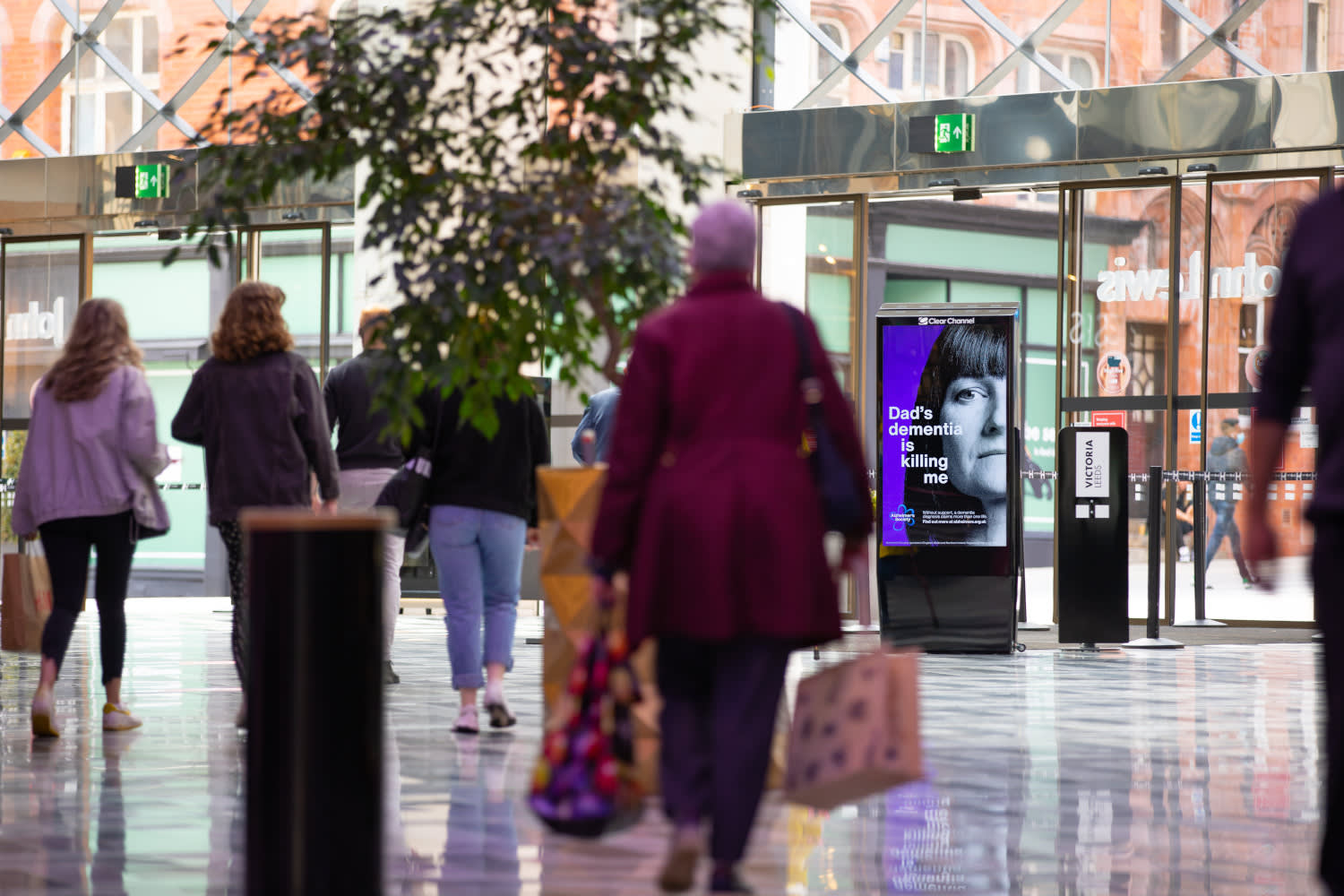 Alzheimer's Society advertising on a Malls Live screen with shoppers walking by
